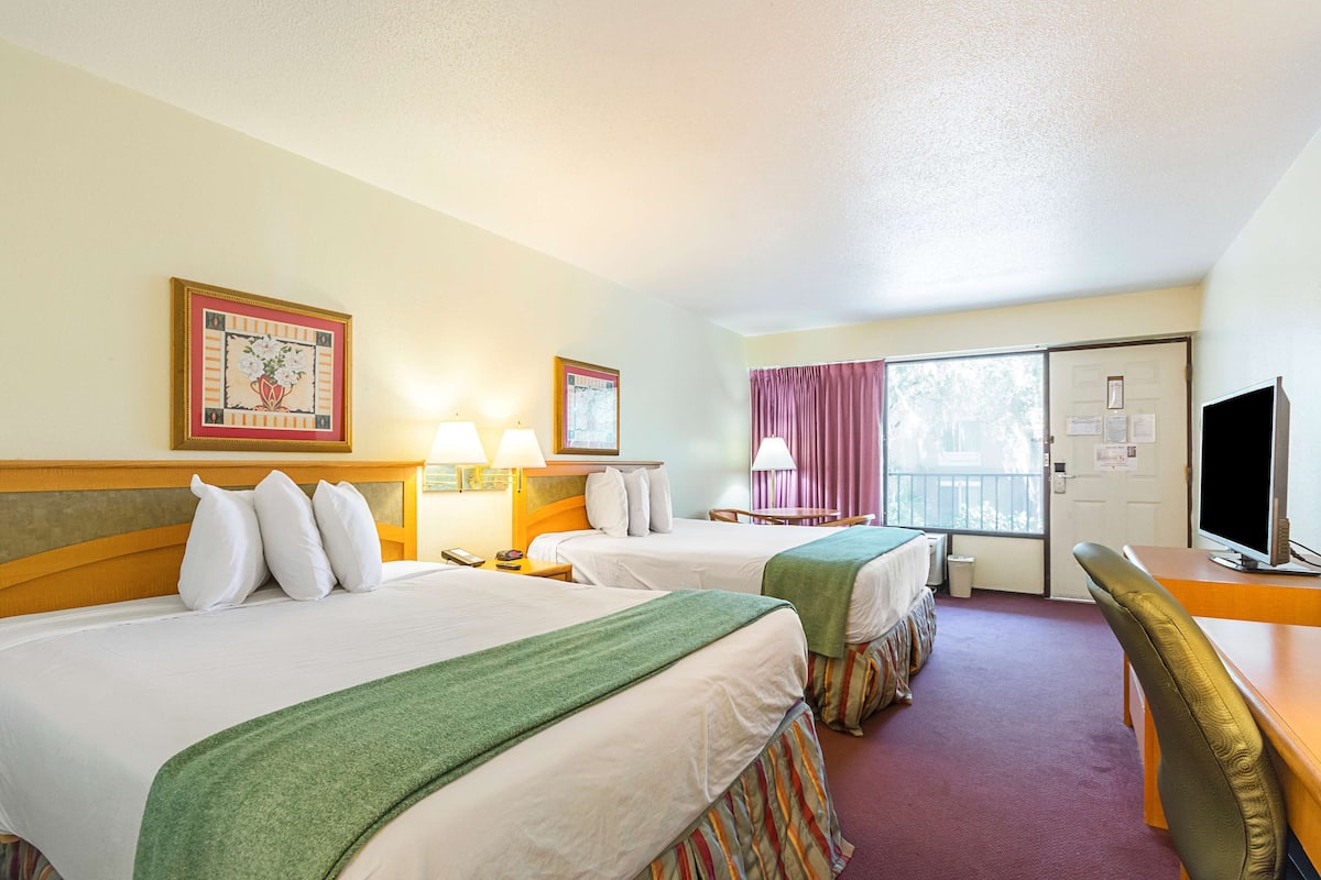 A hotel room with two beds, a desk, a chair, a television, and a window with curtains.