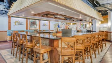 A bar area with a long counter, multiple stools, and a variety of bottles.