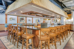A bar area with a long counter, multiple stools, and a variety of bottles.