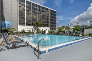 Una piscina con sillas de descanso, un letrero que indica 'no buceo' y un edificio con amplias ventanas al fondo.