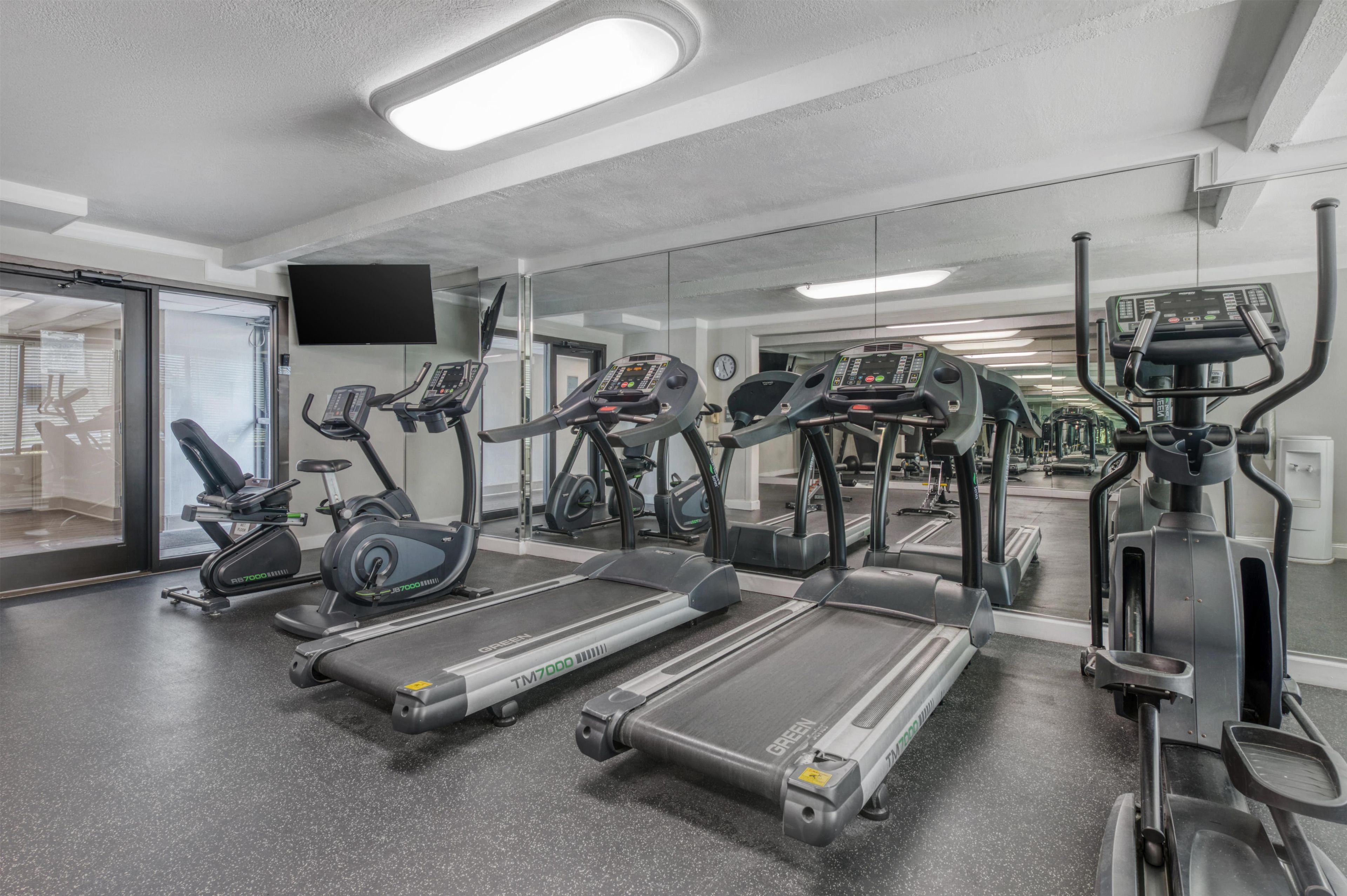 A gym with treadmills, elliptical machines, and a mirrored wall.