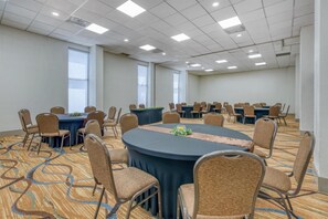 Un salón de conferencias con mesas redondas, sillas y suelo alfombrado.