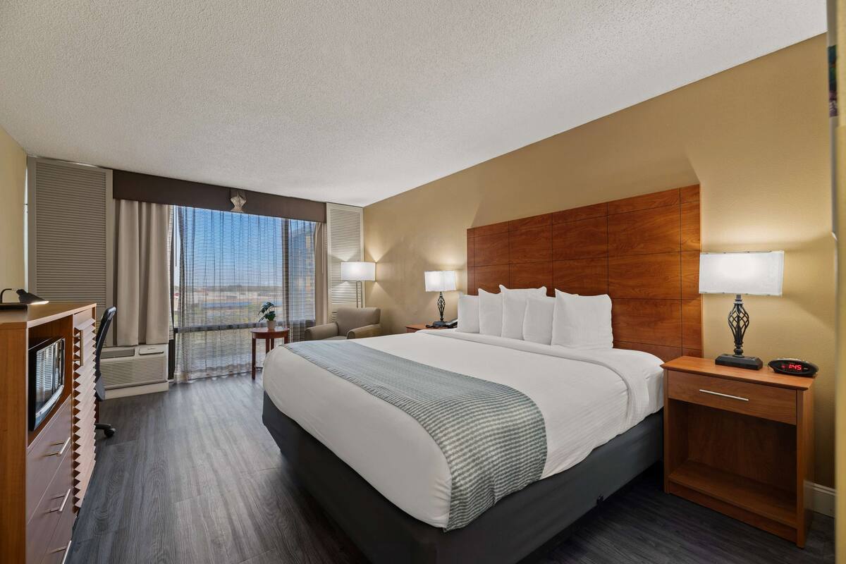 Een hotelkamer met een groot bed, een bureau, een stoel, een nachtkastje en een raam met jaloezieën.