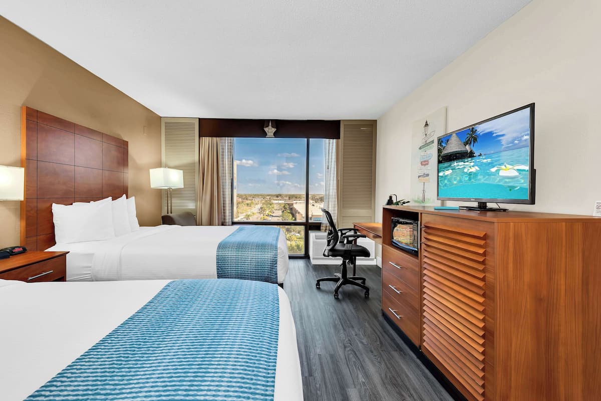 Een hotelkamer met twee bedden, een bureau, een televisie en uitzicht op de stad.