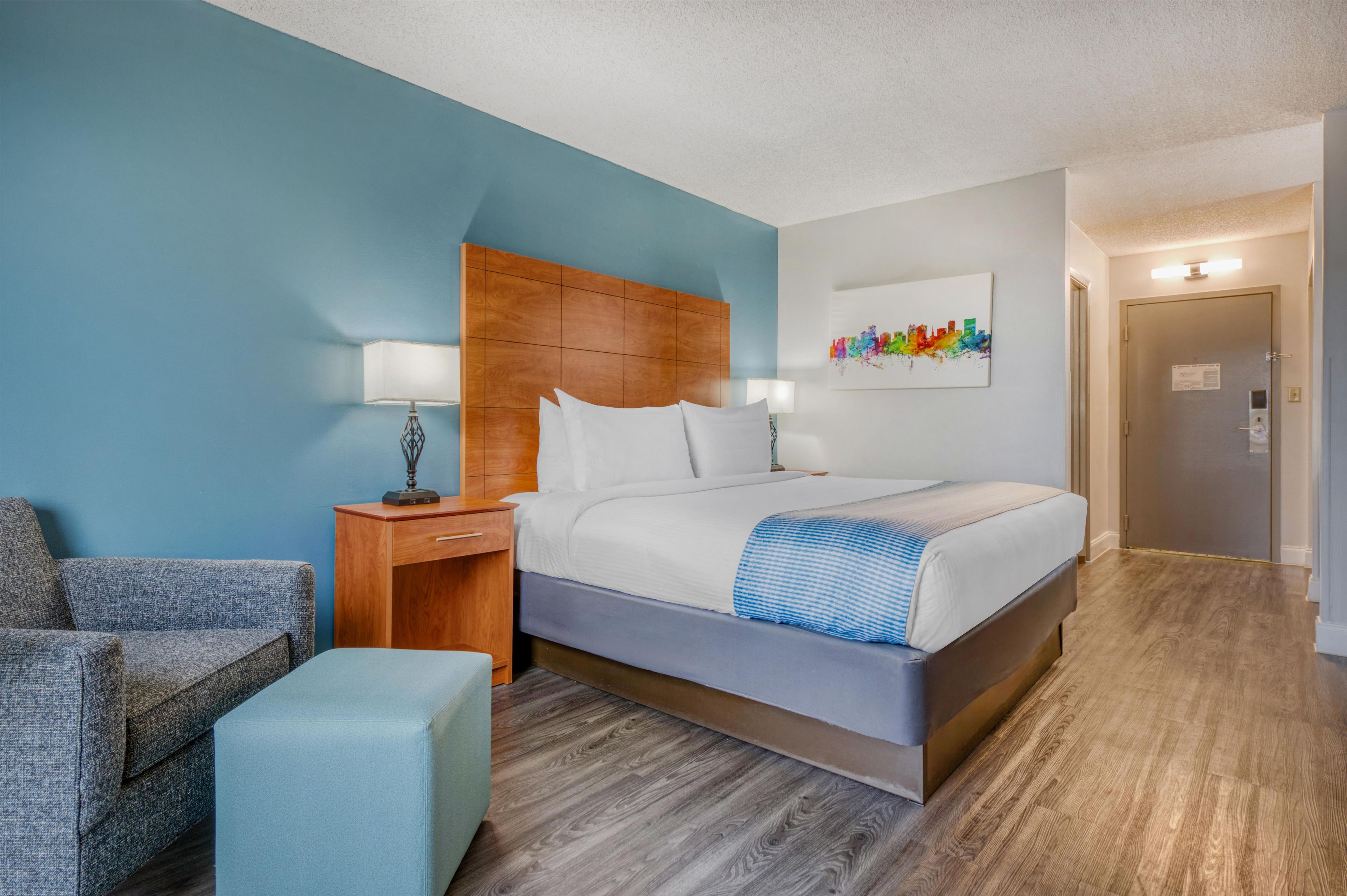 Une chambre d’hôtel avec un lit, une table de chevet, une lampe, une chaise et une porte.