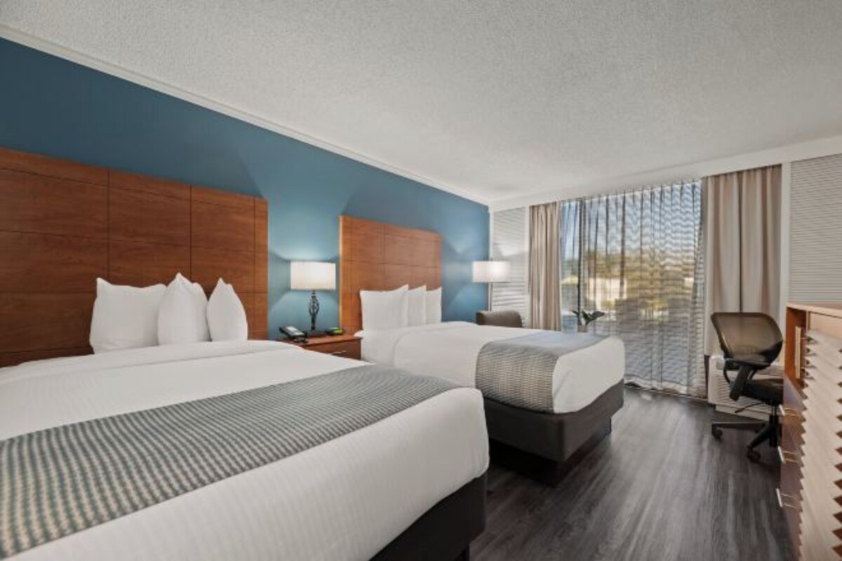 A hotel room with two beds, a desk, a chair, and a window with curtains.