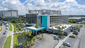 A hotel with a modern glass facade, a parking lot, and a landscaped area with palm trees.