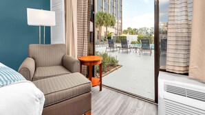 A hotel room with a bed, a chair, a small table, and a view of the outdoor patio with chairs and a pool. - Best Western Orlando Gateway Hotel (Orlando)