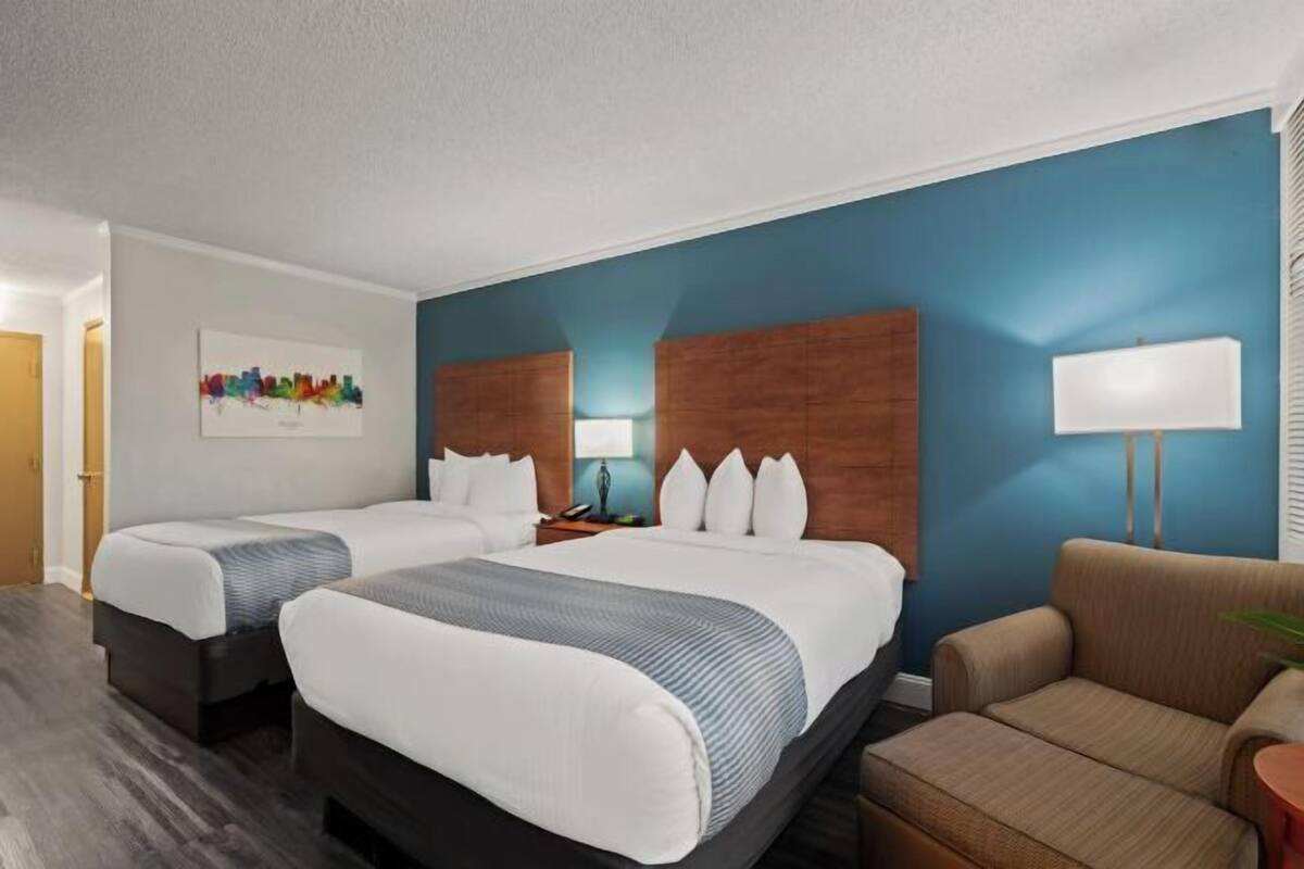 Een hotelkamer met twee bedden, een slaapbank, een lamp en een kunstwerk aan de muur.
