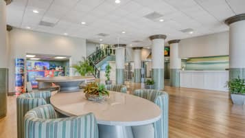 A spacious lobby with a central round table, striped seating, and a staircase leading to upper floors.