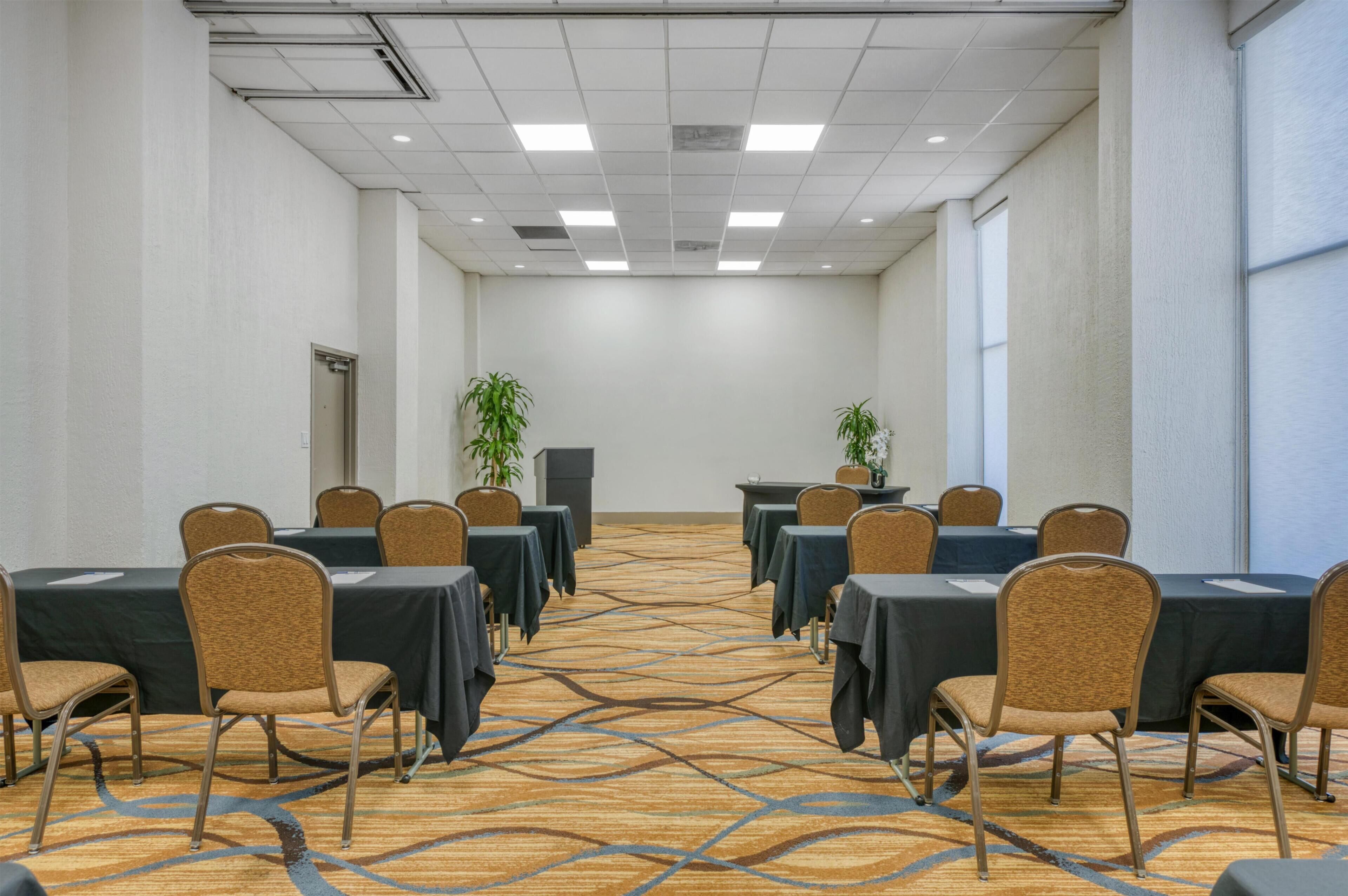 A conference room with tables and chairs, a podium, and potted plants.