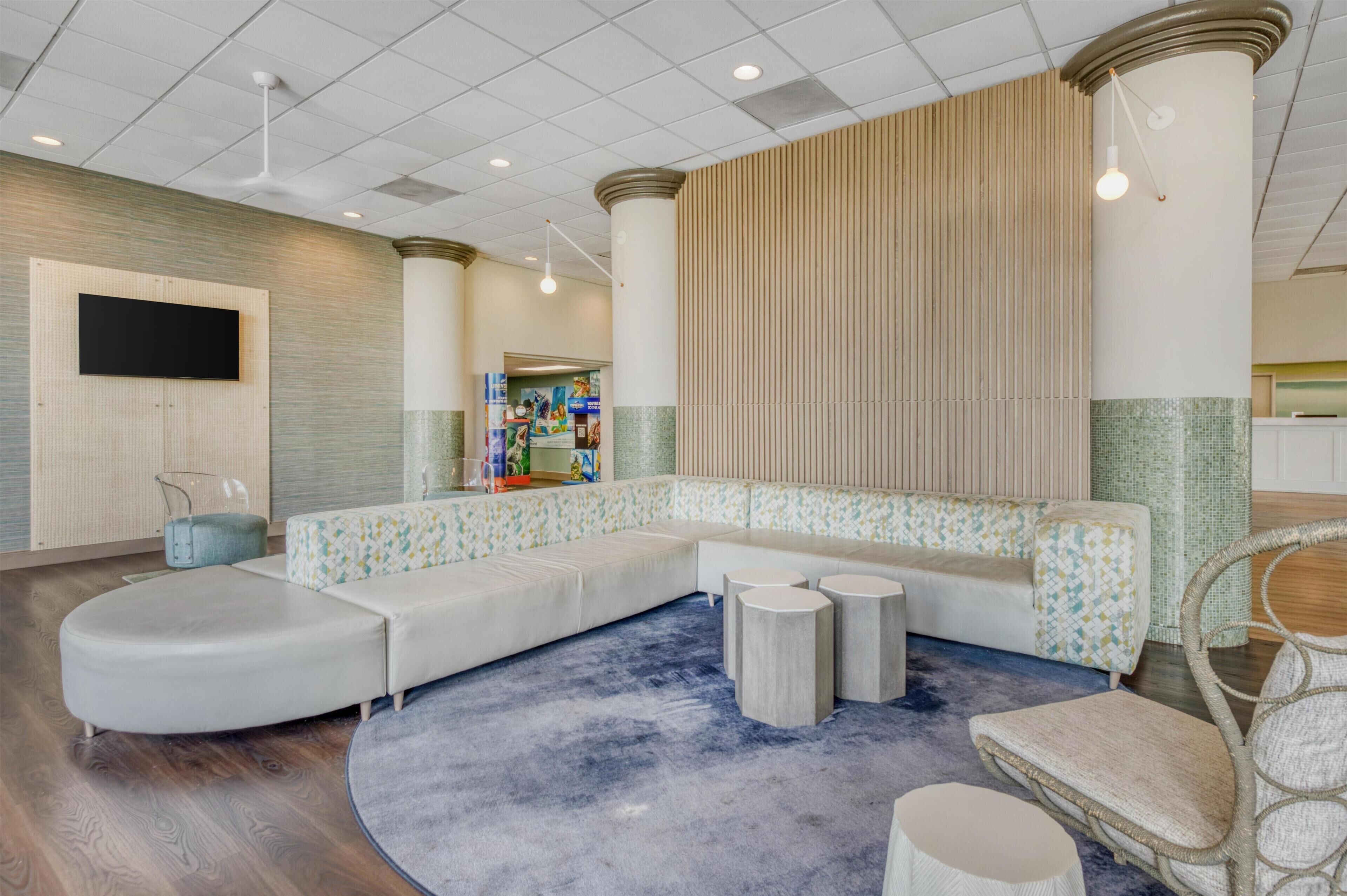 A modern lobby with a curved seating area, a flat-screen TV mounted on the wall, and a patterned wall with vertical lines.