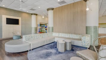 A modern lobby with a curved seating area, a flat-screen TV mounted on the wall, and a patterned wall with vertical lines.