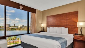 A hotel room with a large bed, a view of a cityscape and water, and a wooden headboard. - Best Western Orlando Gateway Hotel (Orlando)