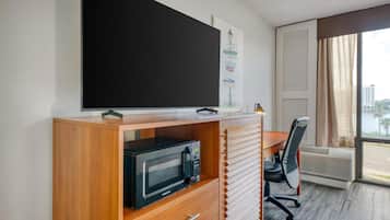 Hotelkamer met een groot flatscreen televisietoestel op een houten kast, een magnetron, een bureau met stoel en een raam met zonwering.