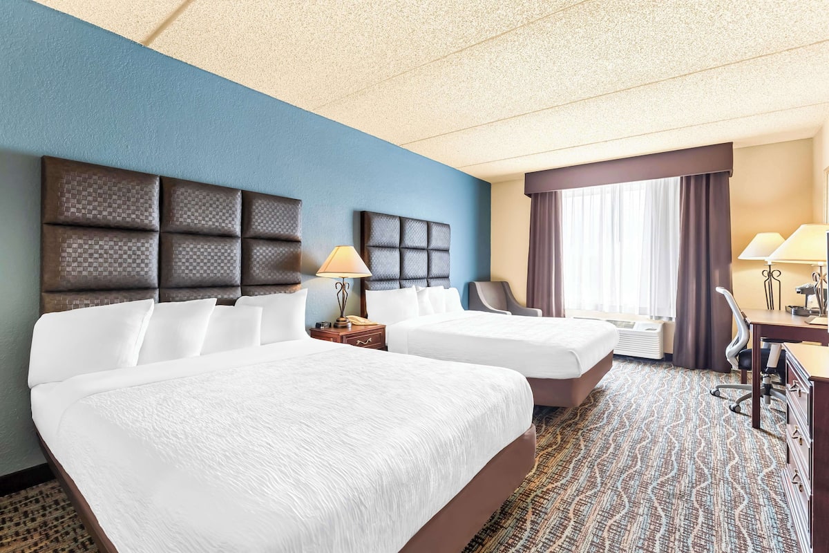 A hotel room with two beds, a desk, a chair, and a window with curtains.