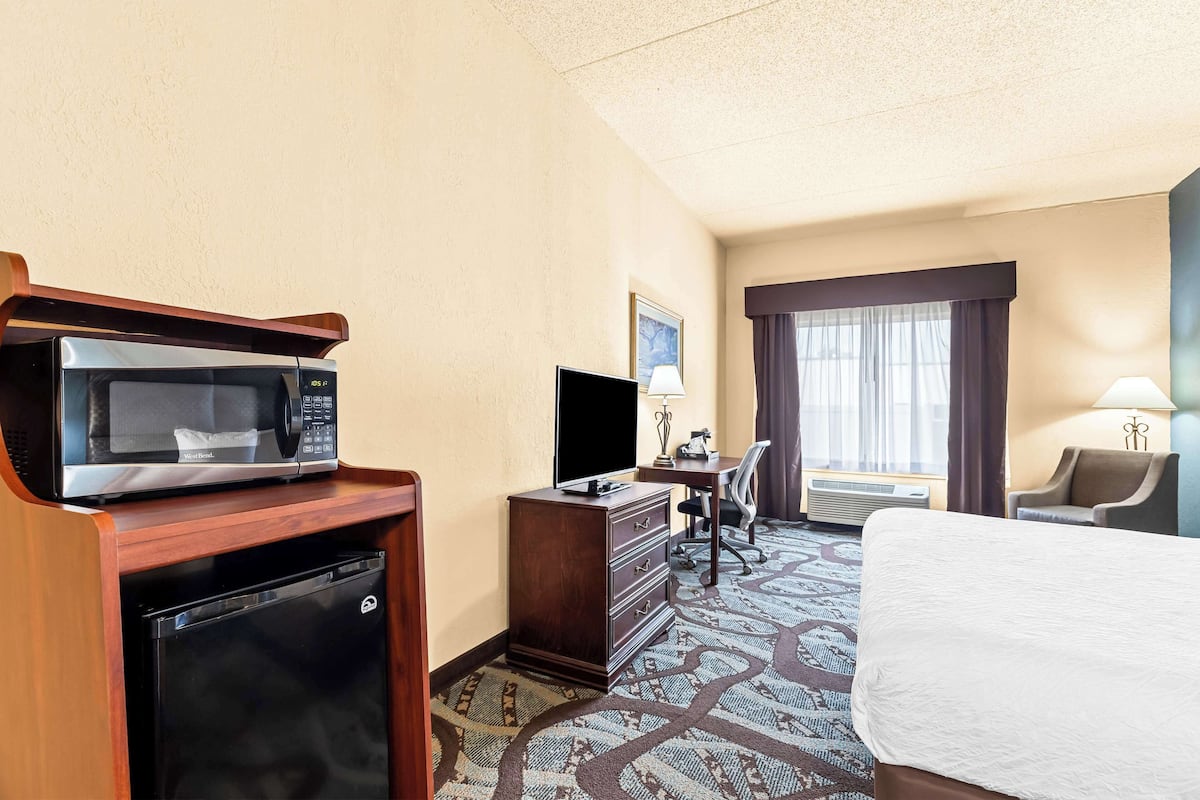 A hotel room with a bed, a desk, a microwave, a refrigerator, a television, and a window with curtains.