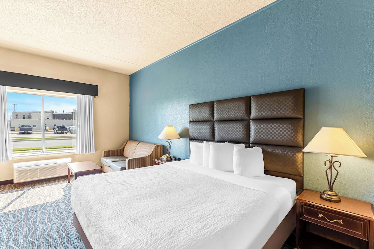 A hotel room with a large bed, a sofa, a desk, and a window with a view of the street.