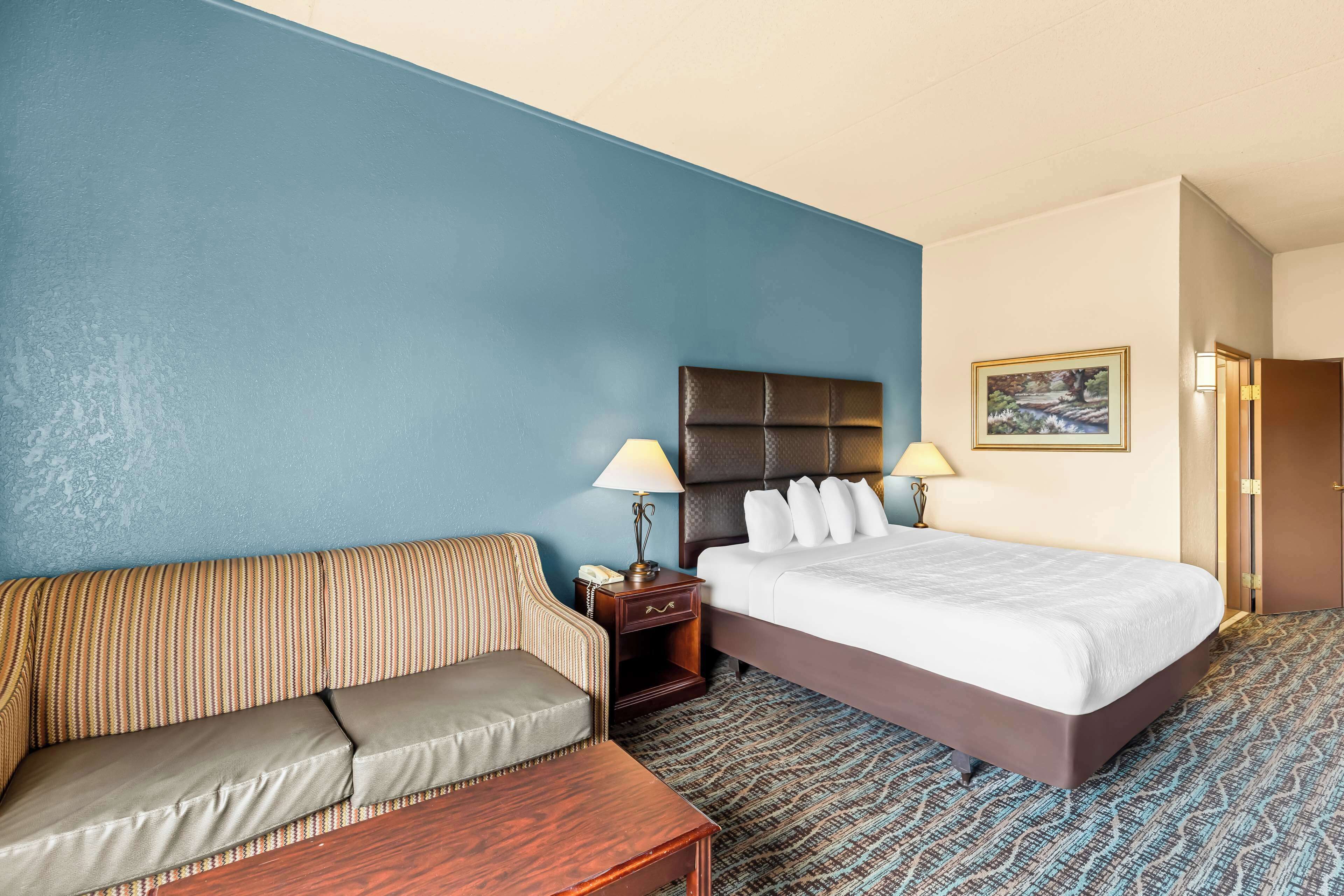 A hotel room with a bed, a sofa, a nightstand, and a lamp.