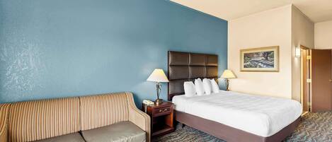 A hotel room with a bed, a sofa, a nightstand, and a lamp.