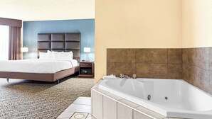 A hotel room with a large bed, a separate bathroom with a bathtub, and a nightstand with a lamp. - Best Western Holiday Manor (Newton)
