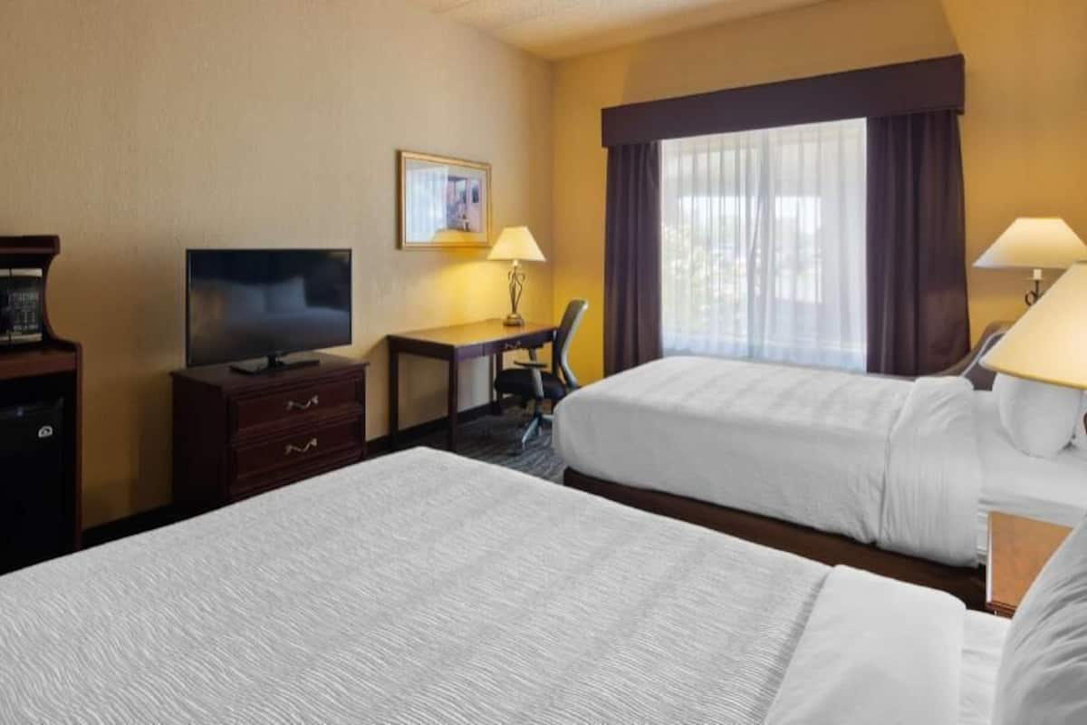 A hotel room with two beds, a desk, a television, and a window with curtains.