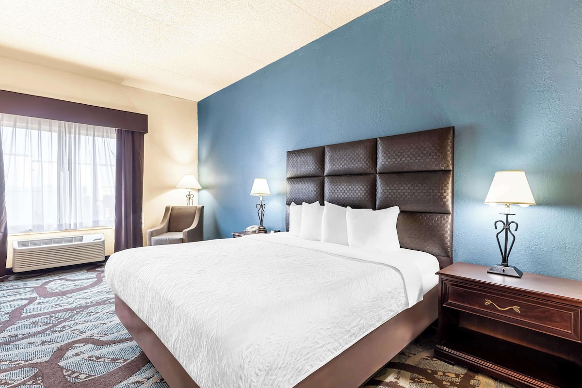 A hotel room with a large bed, two bedside lamps, a chair, and a desk.
