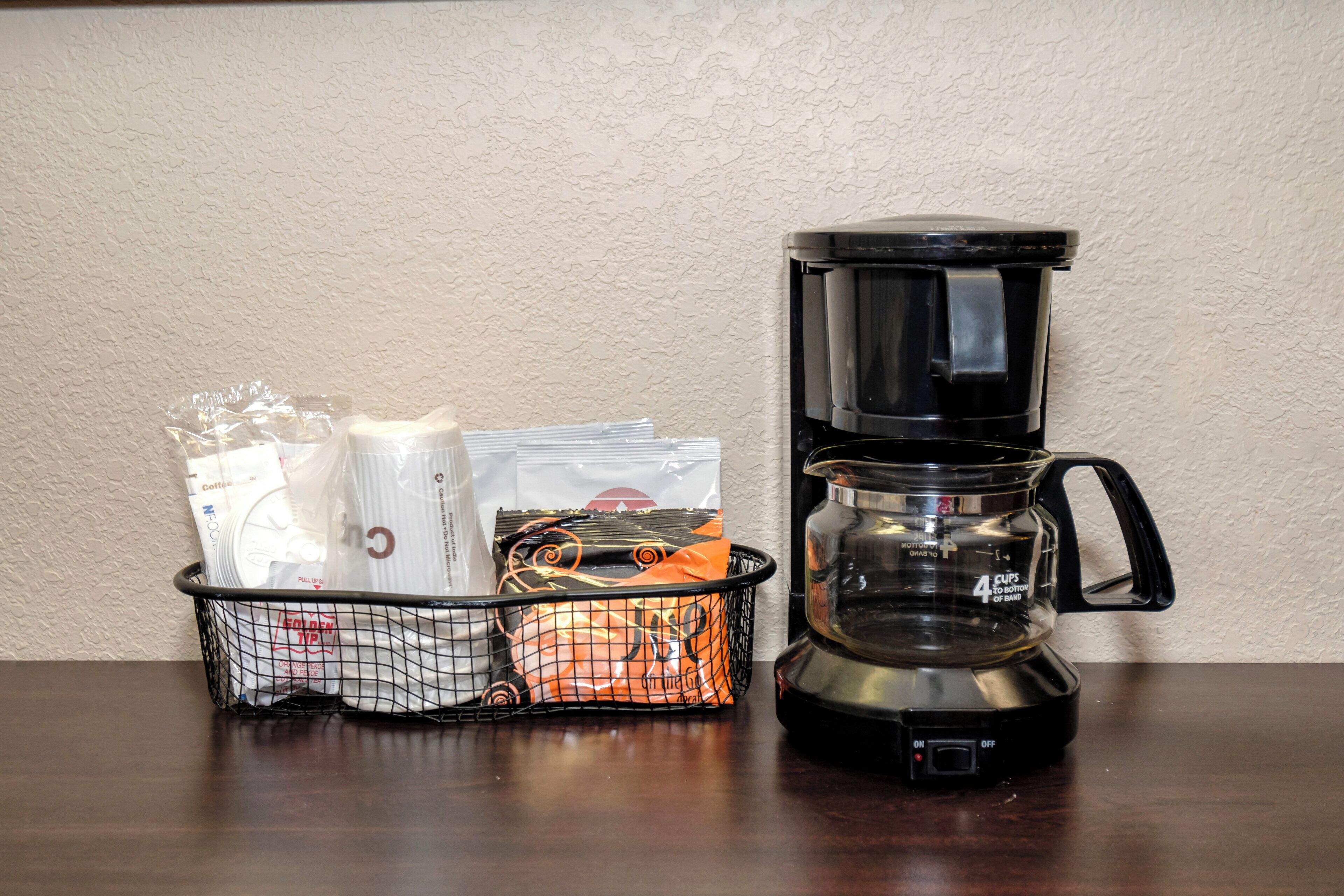 A coffee maker and a basket with coffee packets on a wooden table.