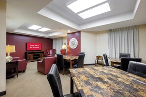 Un salón de conferencias con una gran mesa, sillas, un televisor que muestra 'Wi-Fi gratis en todas las habitaciones' y un elemento decorativo en la pared.