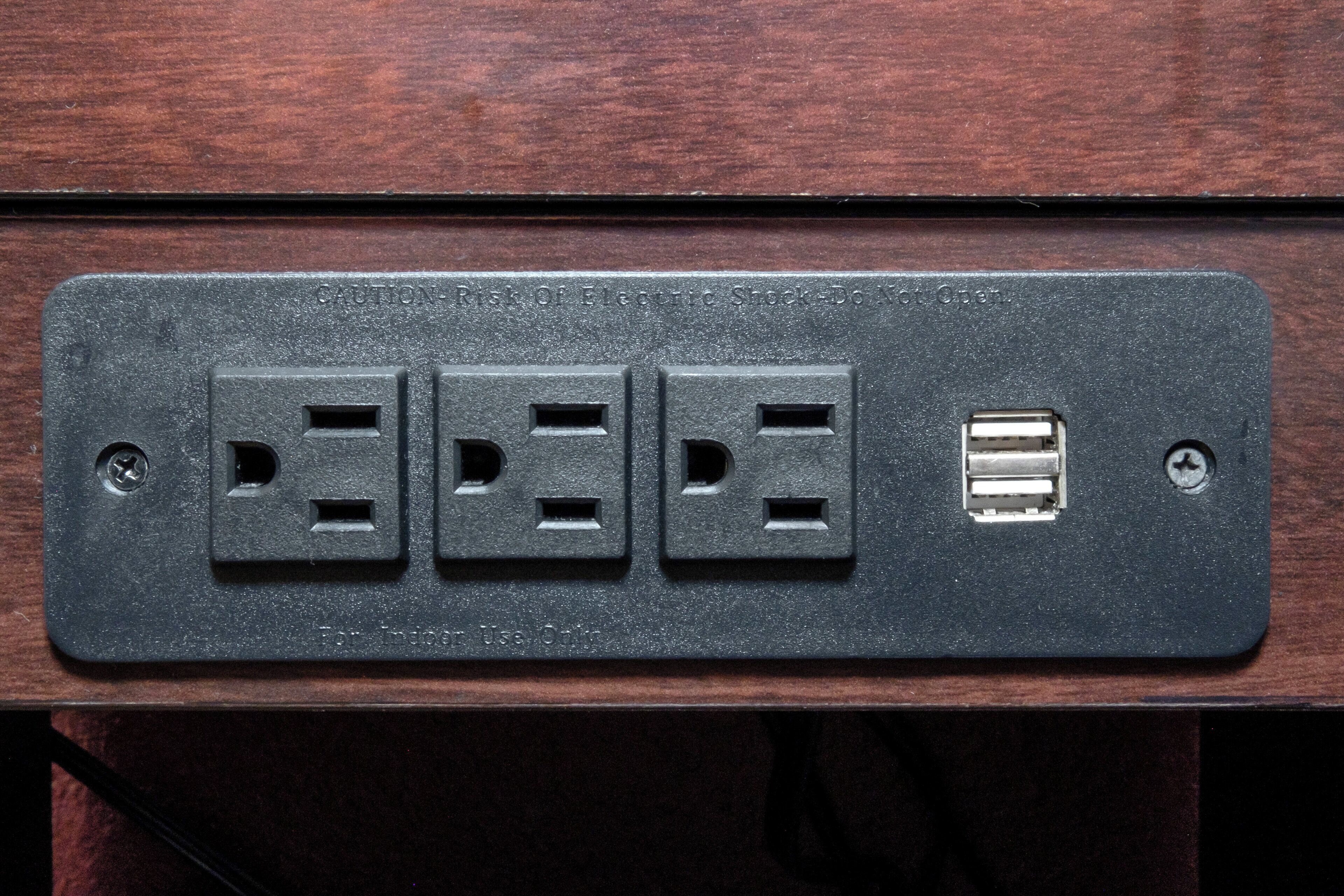 Eine schwarze Steckdose mit drei Standardsteckplätzen und einem USB-Anschluss auf einer Holzoberfläche.