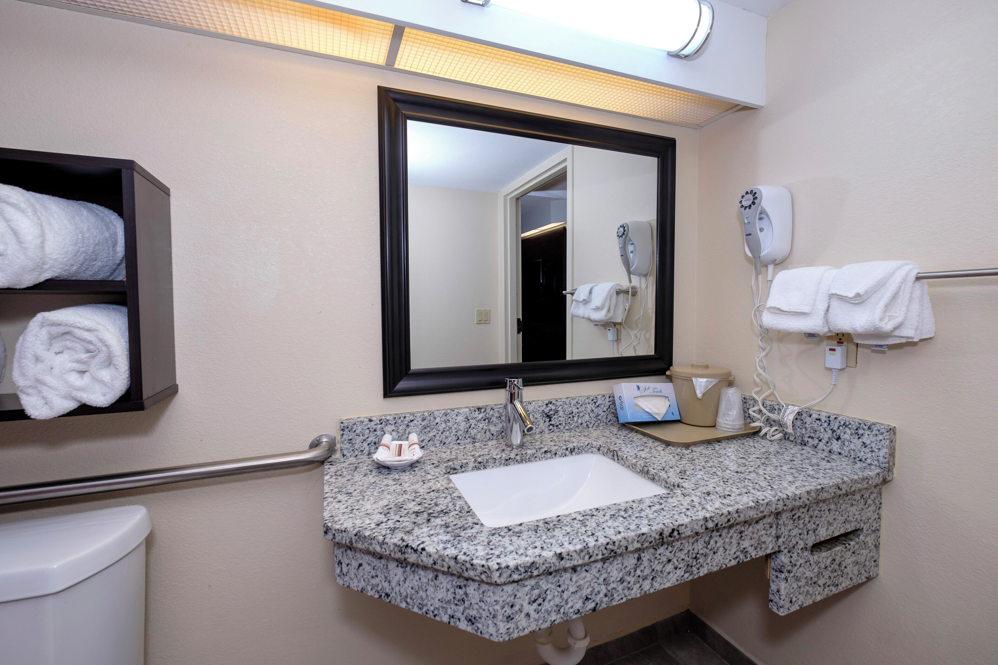 A bathroom with a granite countertop, a sink, a mirror, a towel rack, and a hand dryer.