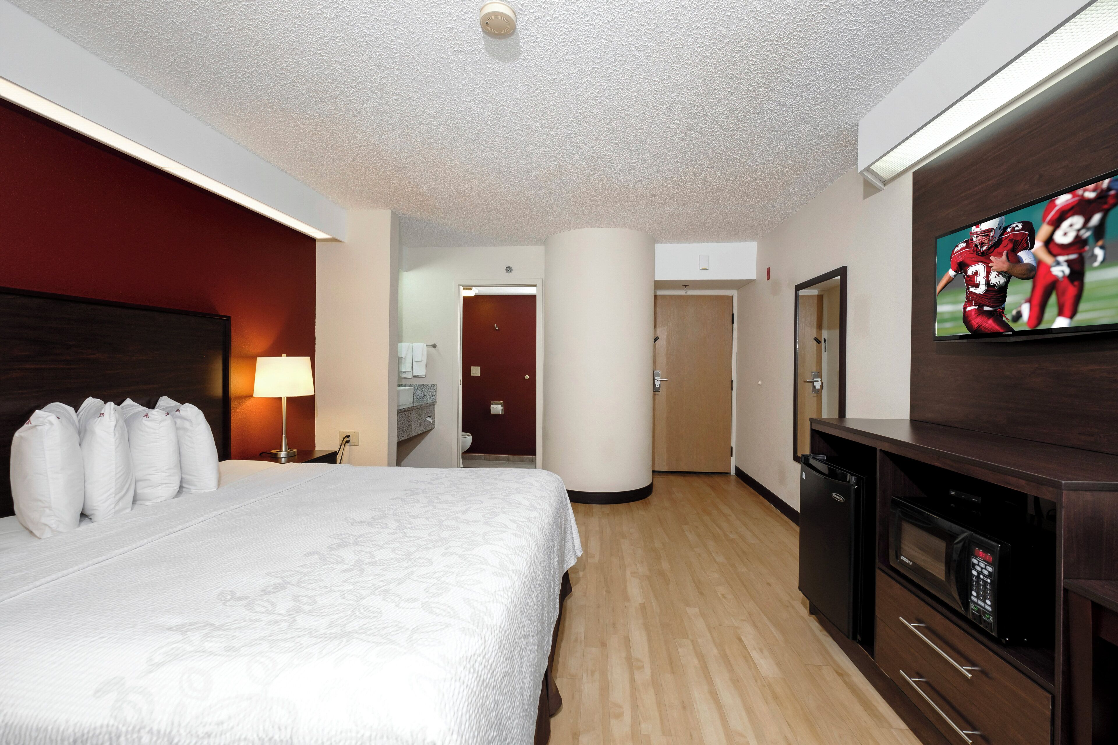 Une chambre d’hôtel avec un lit, une télévision, un bureau et une salle de bain visible à travers une porte ouverte.