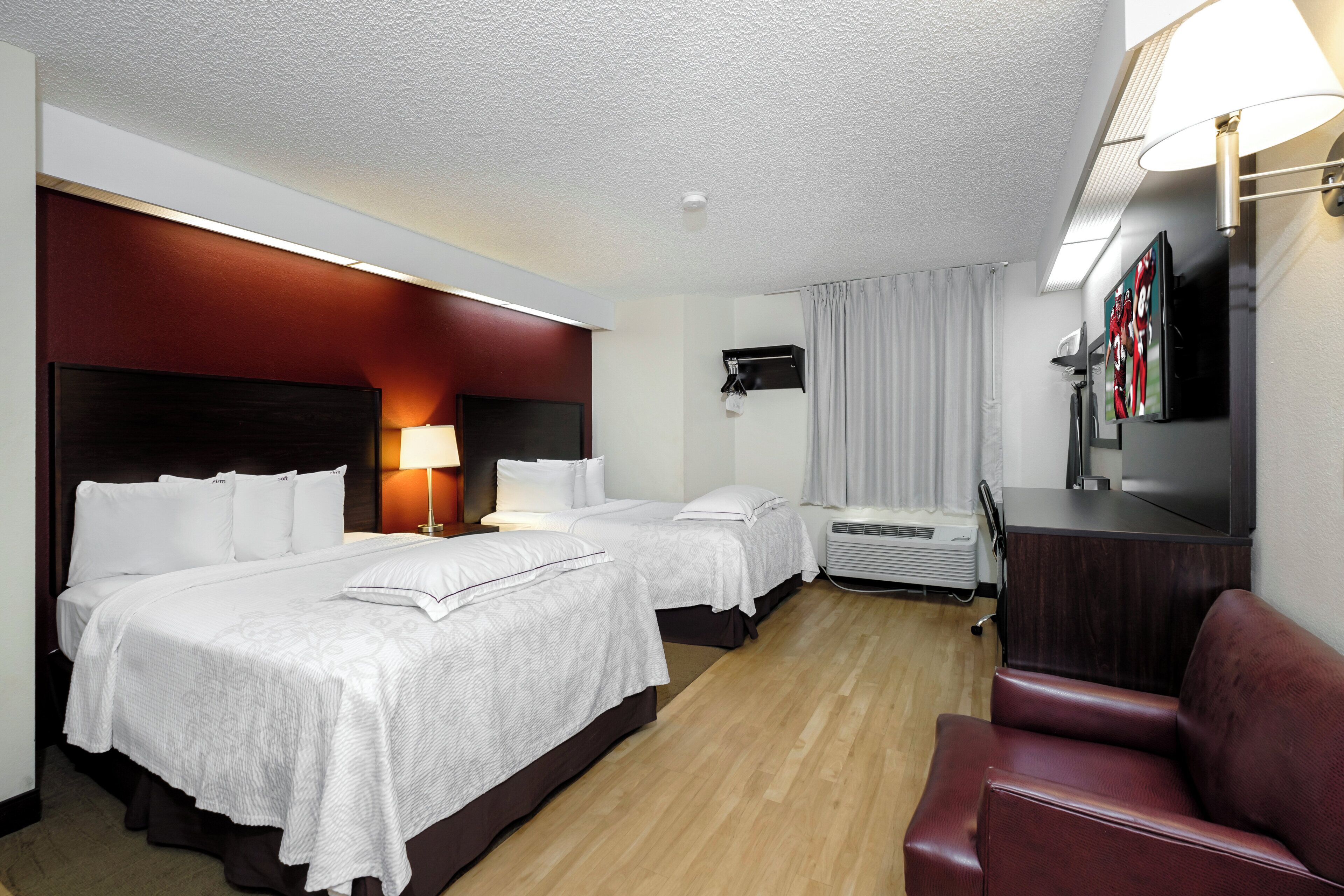 A hotel room with two beds, a desk, a TV, and a seating area.