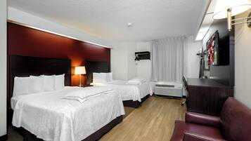 A hotel room with two beds, a desk, a TV, and a seating area.