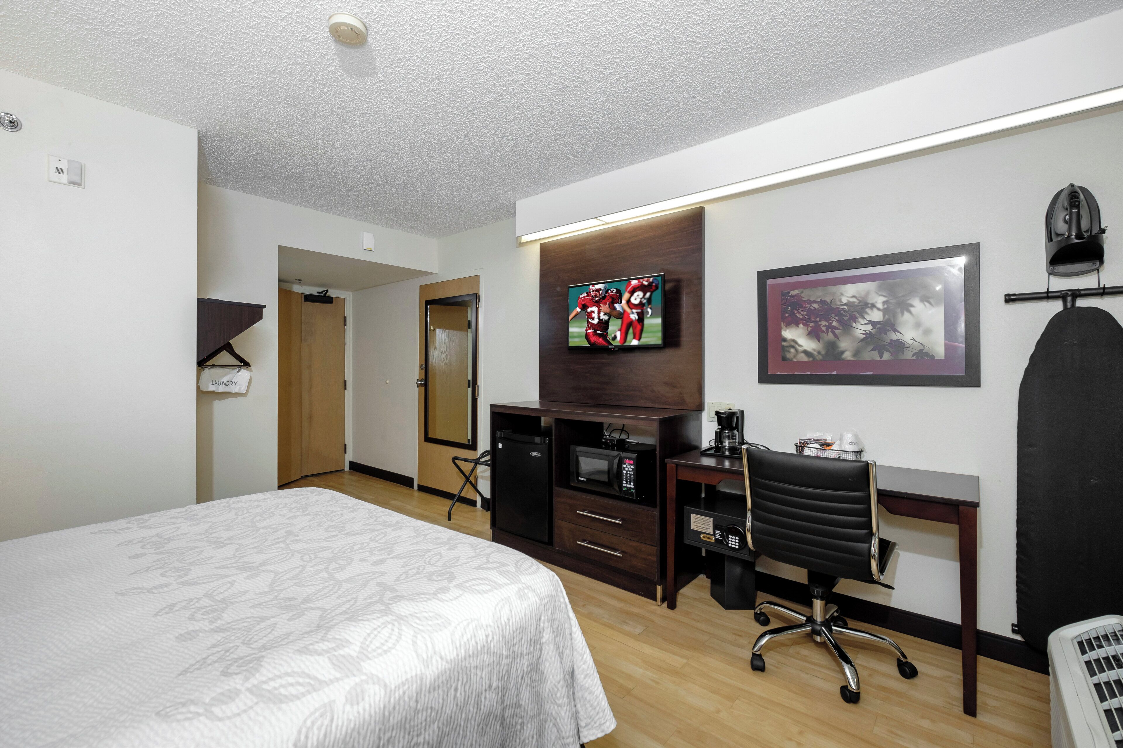 A hotel room with a bed, a desk, a chair, a television, and a coffee machine.