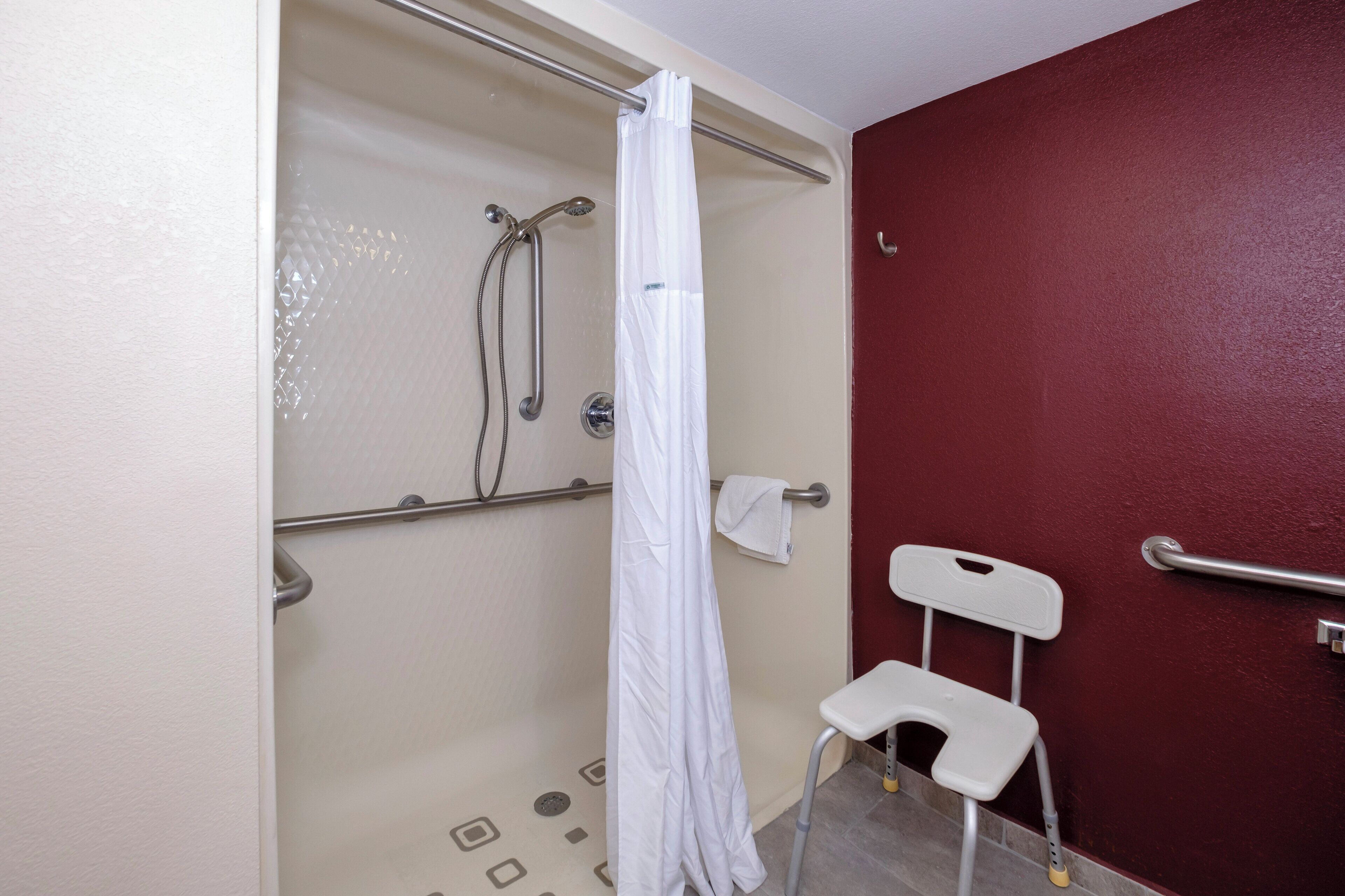 A shower area with a white shower curtain, a grab bar, and a white chair.