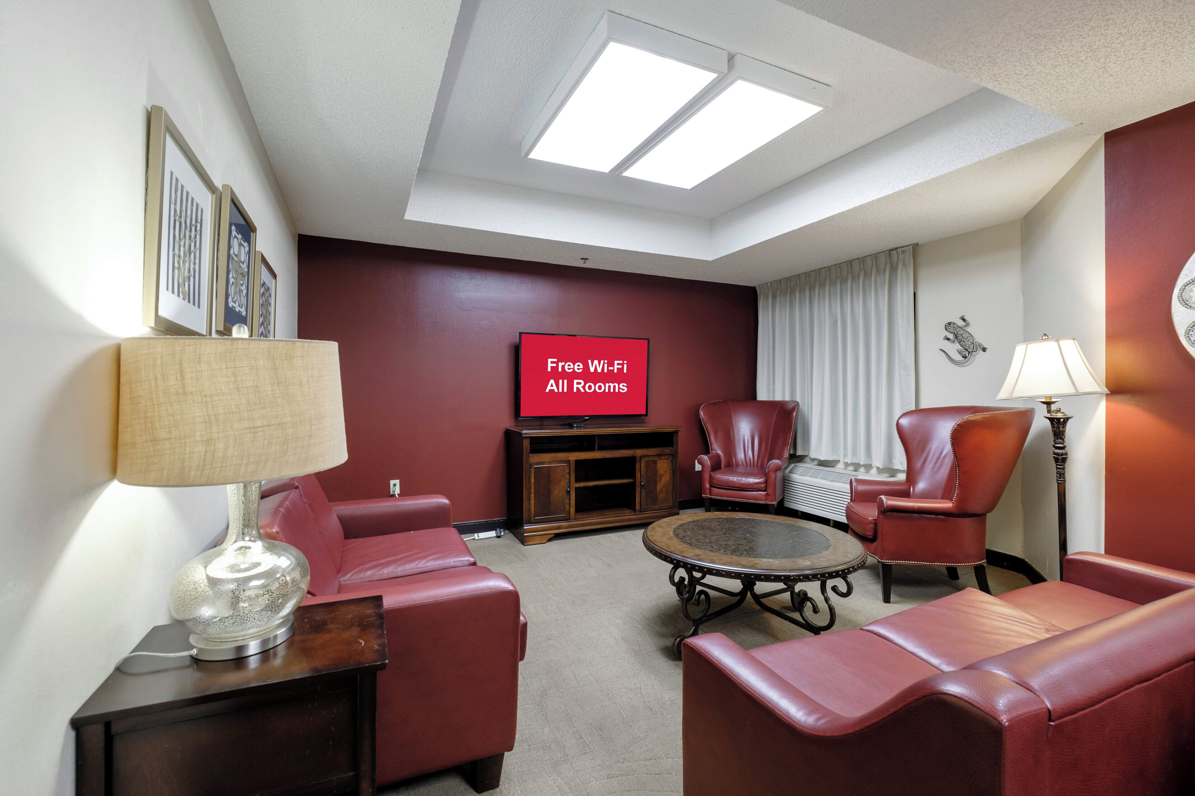 A hotel room with a red sofa, a leather armchair, a small coffee table, and a flat-screen TV displaying 'Free Wi-Fi All Rooms'.