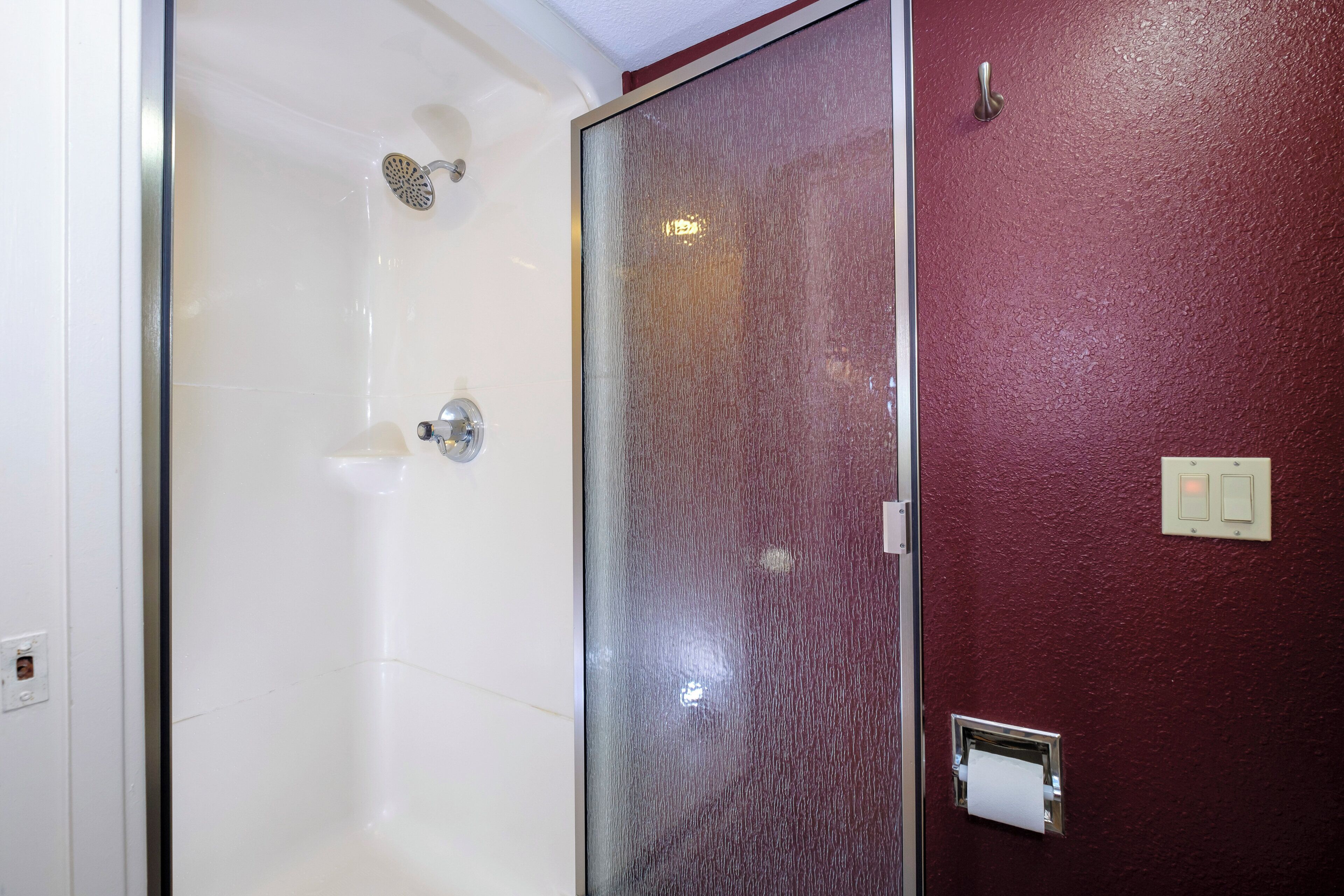 A bathroom with a glass shower enclosure, a white tiled wall, and a red textured wall.