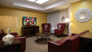 A hotel room with a TV, leather chairs, a small table, a lamp, and a decorative mirror. - Red Roof Inn PLUS+ Palm Coast (Palm Coast)