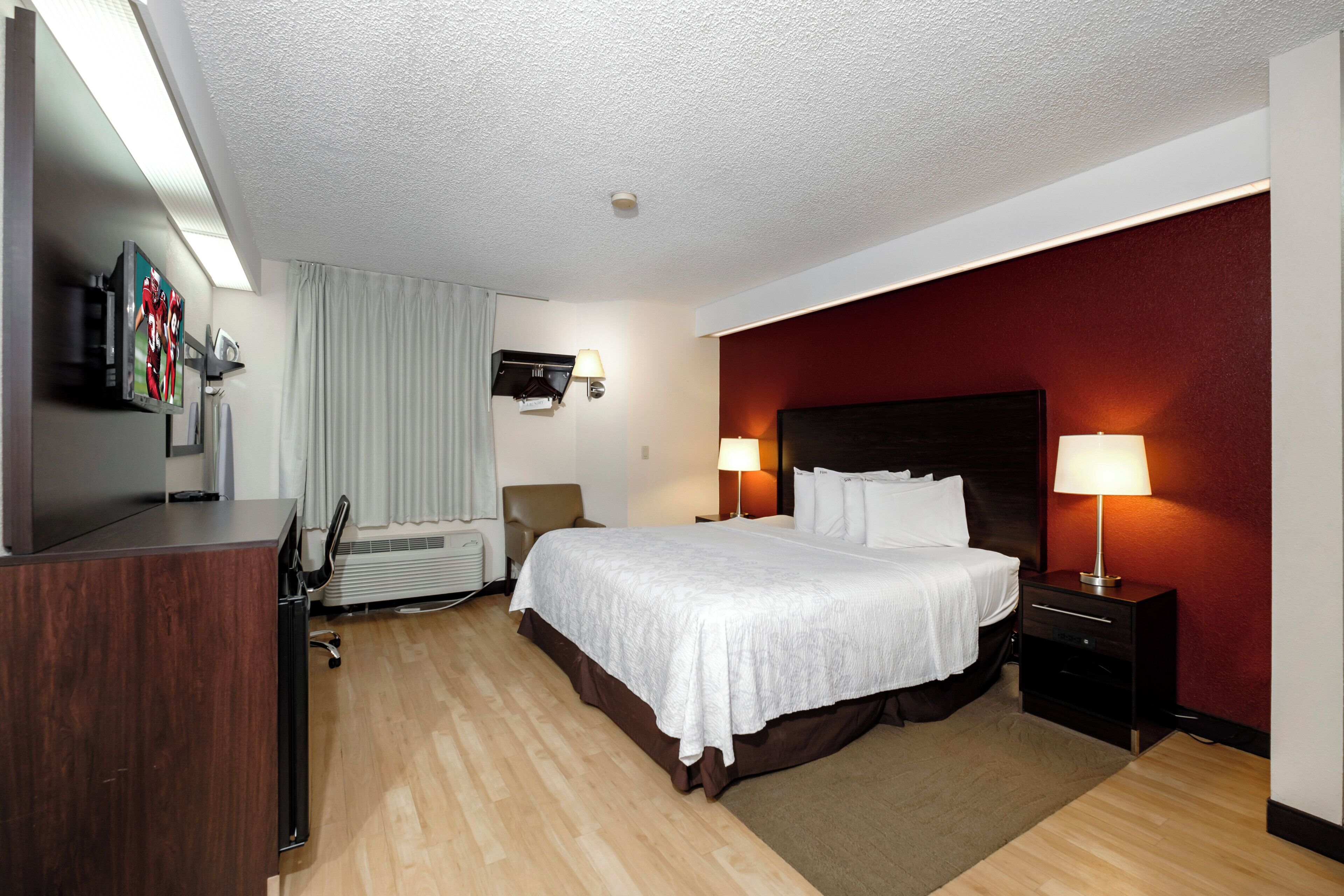 Quarto de hotel com cama, luminárias de cabeceira, televisão, escrivaninha e uma cadeira.