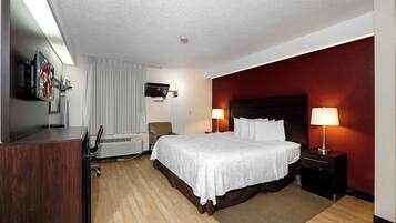 Quarto de hotel com cama, luminárias de cabeceira, televisão, escrivaninha e uma cadeira.