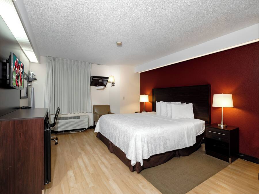 Quarto de hotel com cama, luminárias de cabeceira, televisão, escrivaninha e uma cadeira.