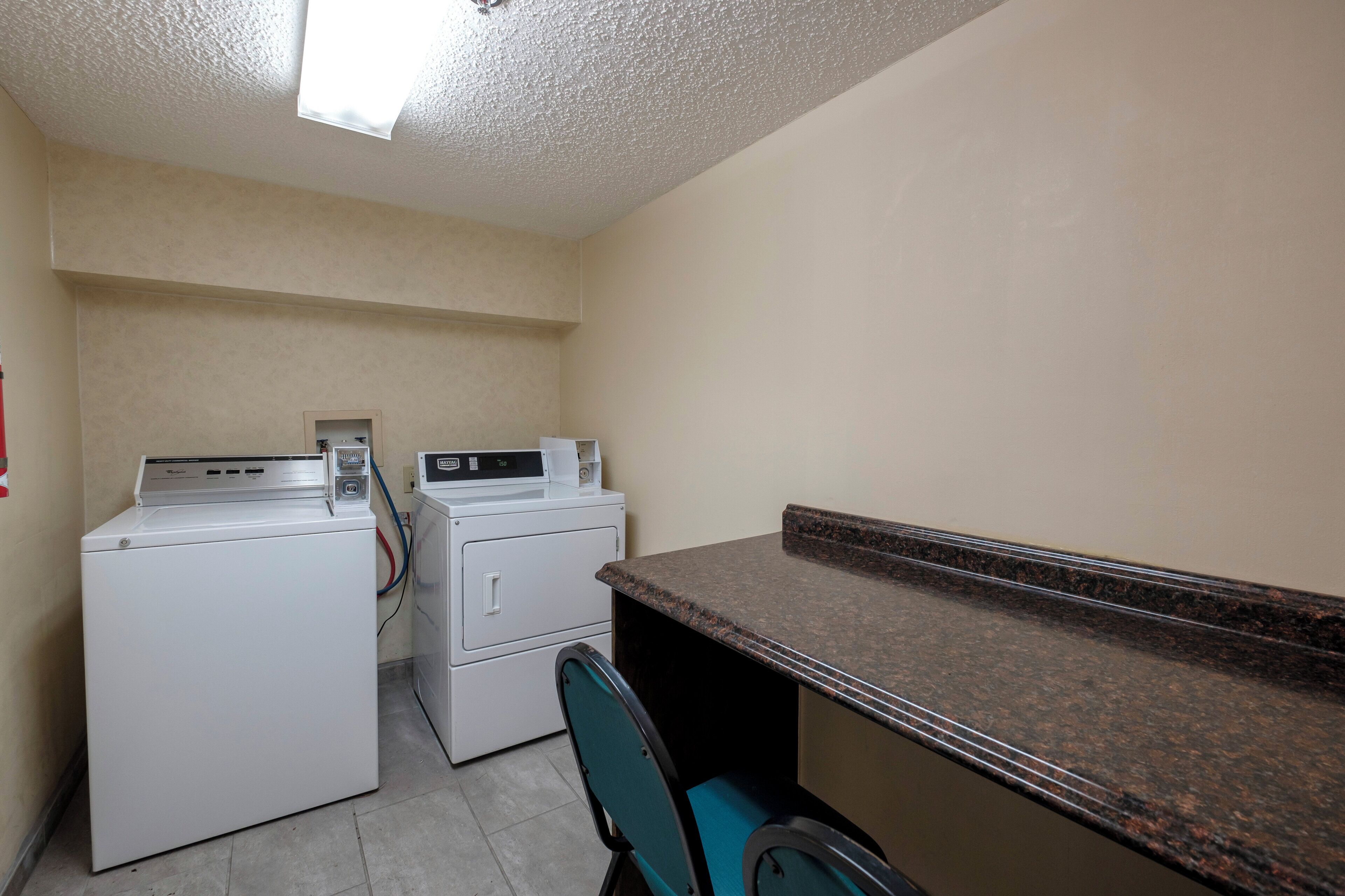 A laundry room with two white washing machines, a dryer, and a countertop with a sink.