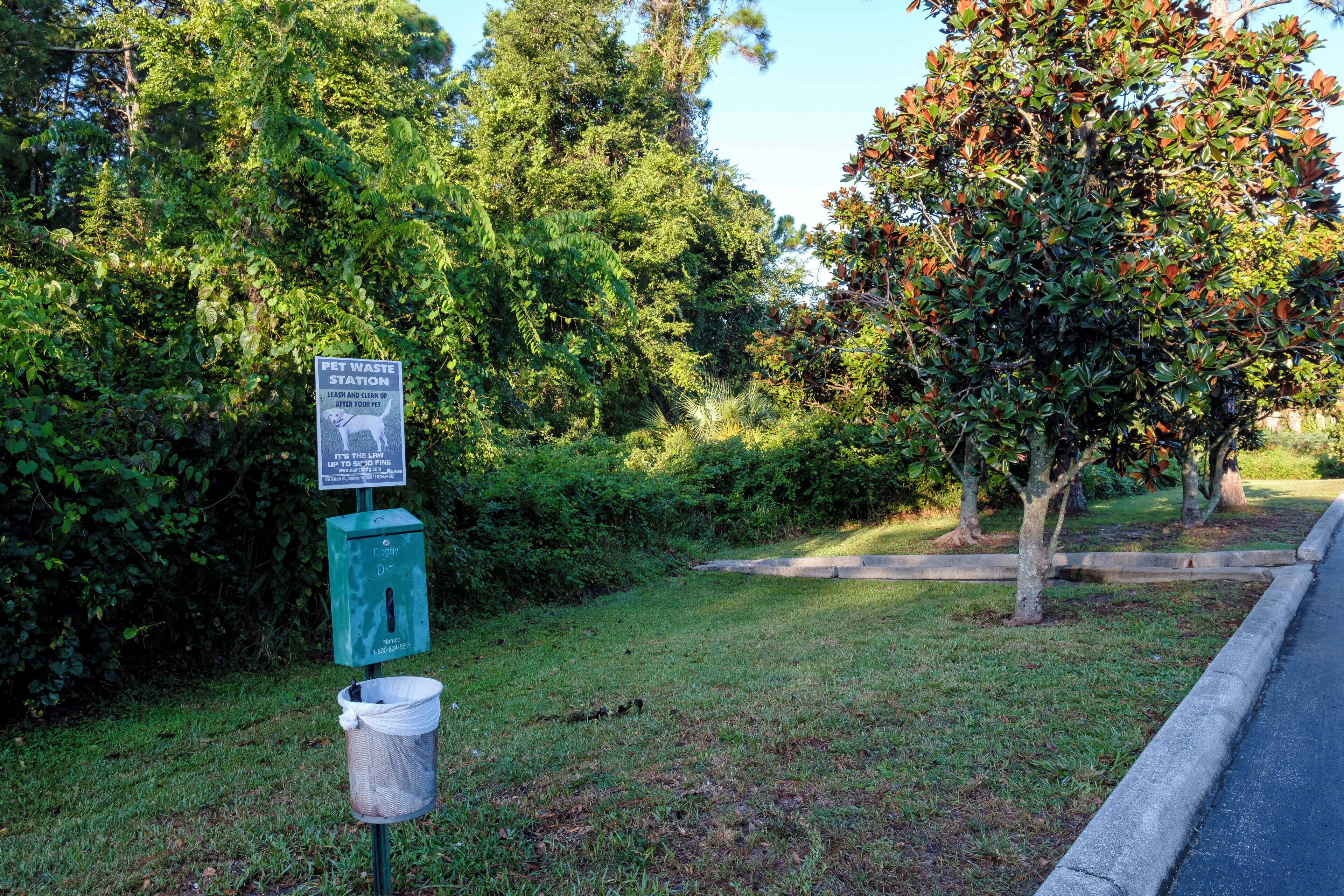 A pet waste station with a trash bin and a sign.