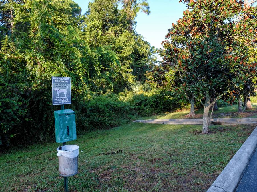 A pet waste station with a trash bin and a sign.
