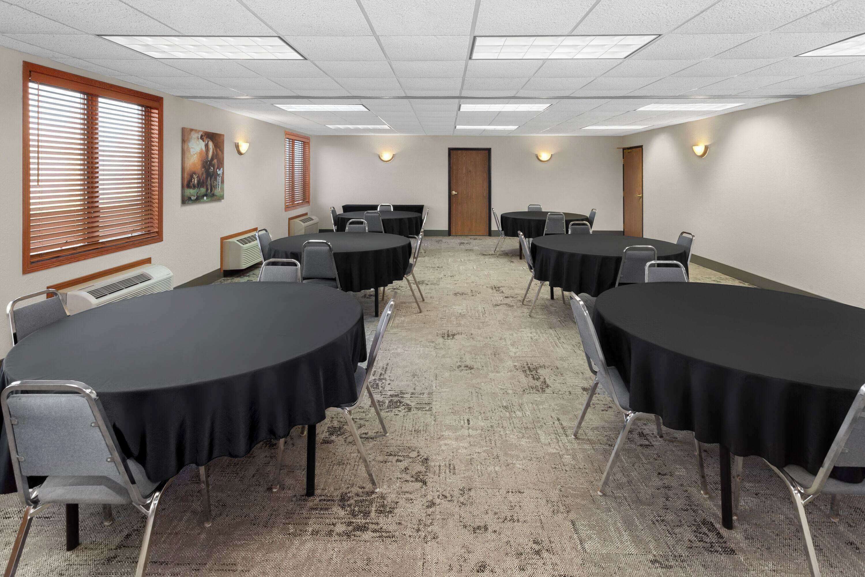 A conference room with round tables, chairs, and carpeted flooring.
