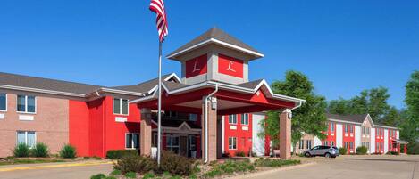 A red-brick building with a prominent American flag, a covered entrance, and a parking lot.