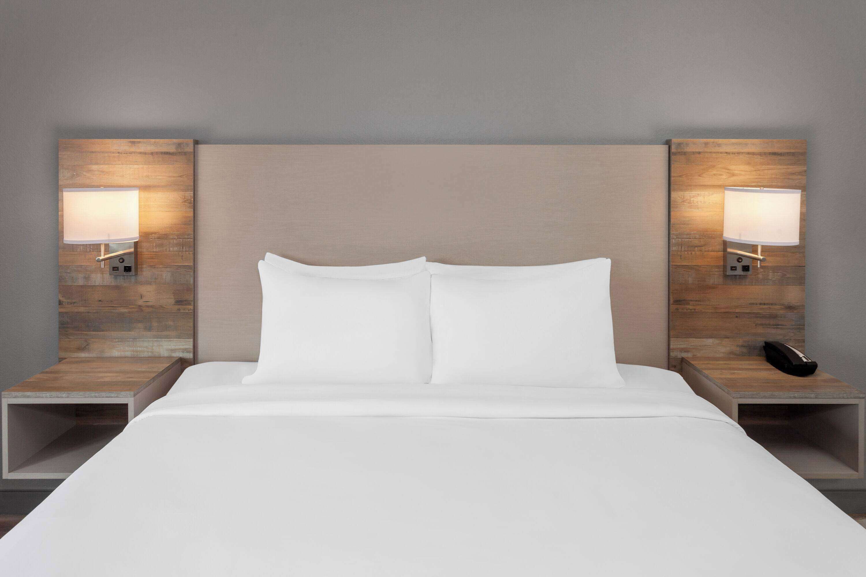 A modern hotel room with a large bed, two bedside tables, and wall-mounted lamps.