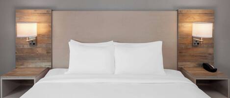 A modern hotel room with a large bed, two bedside tables, and wall-mounted lamps.