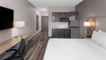 Habitación de hotel con cama, escritorio, silla, televisor, microondas, refrigerador y una pequeña kitchenette.